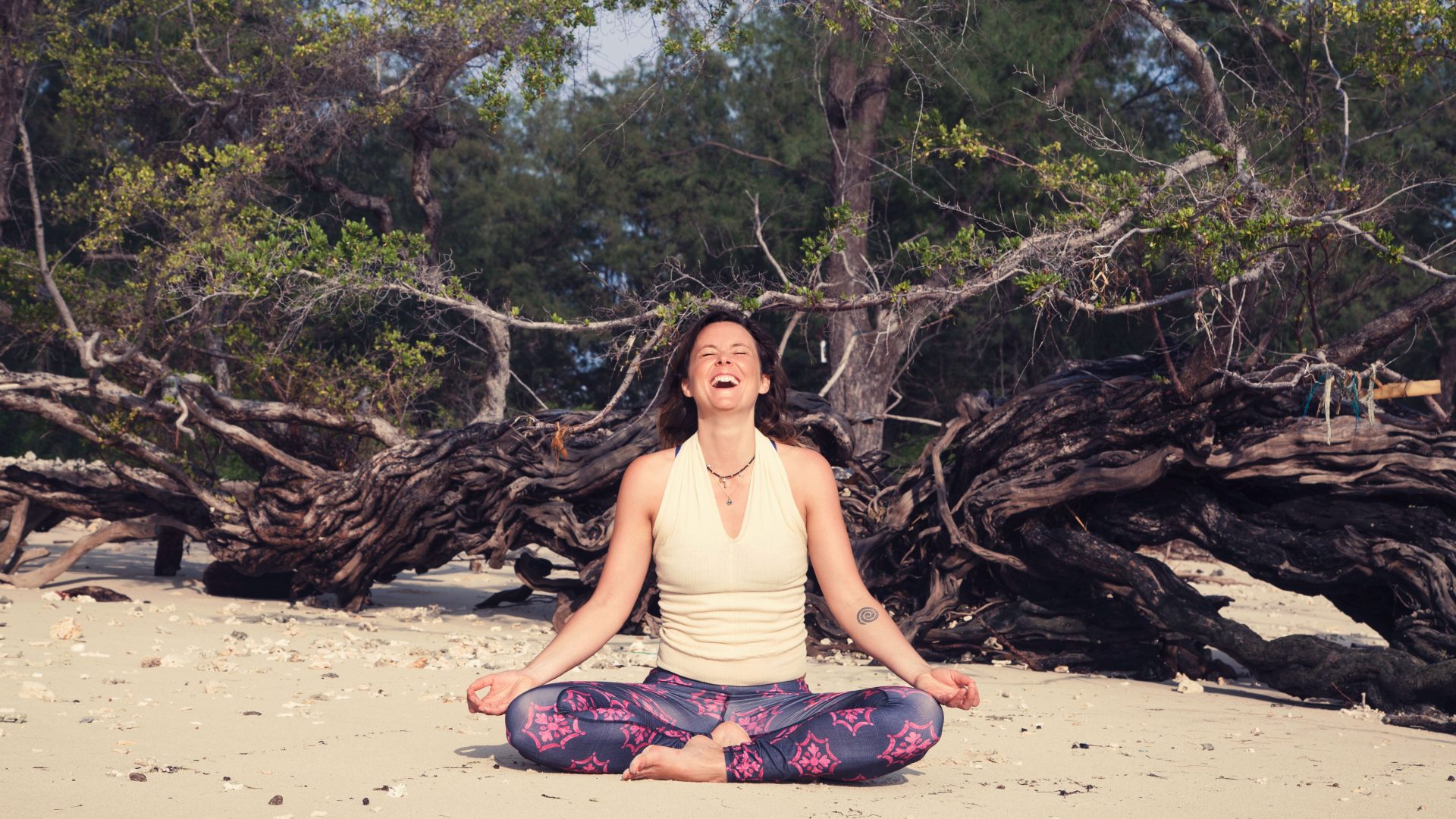 Meget glad kvinde på en strand, som sidder i en yoga lotusstilling